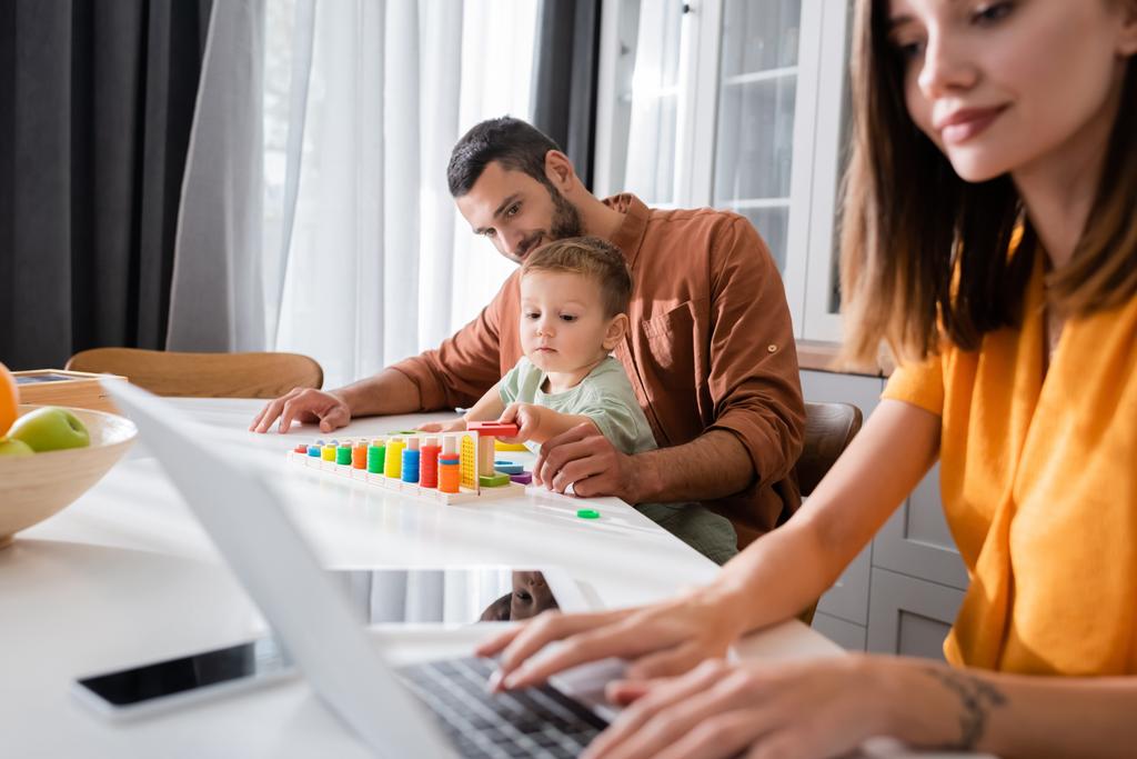 Man and kid playing educational game near mother using laptop