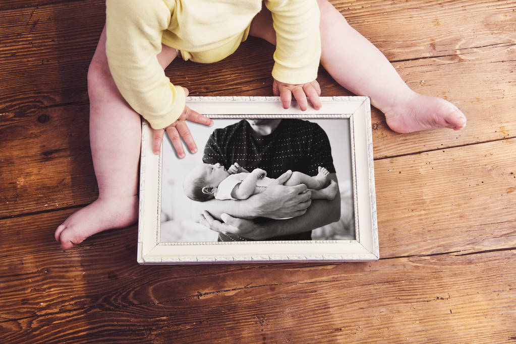 little baby holding picture frame with picture of father and son